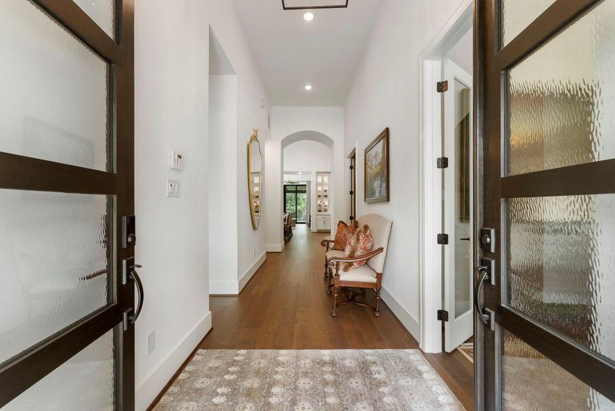 Double entry doors open to a bright, refined foyer with wood flooring and an immediate sense of custom detail. The upgraded glass and transom-style accents help set the tone for the home’s elevated finish level.