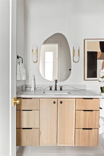 Vanity with a light wood finish, integrated sink, and stone countertop