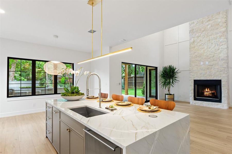 Kitchen with stainless steel dishwasher, light wood-style floors, a kitchen island with sink, light stone countertops, and hanging light fixtures