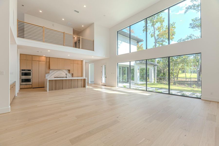 This spacious, modern home features an open-concept kitchen with sleek wood cabinetry and a large island. The living area boasts high ceilings and expansive windows, offering abundant natural light and stunning views of the outdoors. Perfect for those seeking a bright and airy living space.