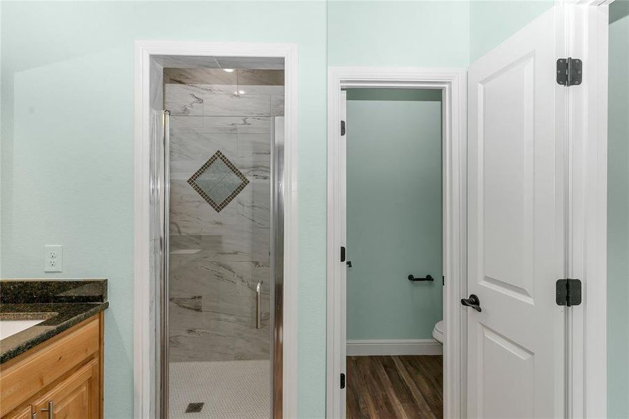 Full bath with a marble finish shower, vanity, and dark wood-type flooring