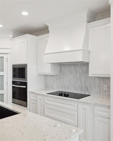 Kitchen featuring white cabinets, light stone countertops, tasteful backsplash, and stainless steel appliances