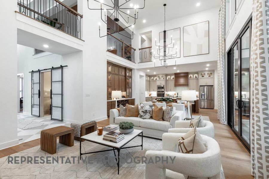 Living room with a chandelier, a towering ceiling, a barn door, light wood-style floors, and baseboards Living room with a chandelier, a towering ceiling, a barn door, light wood-style floors, and baseboards
