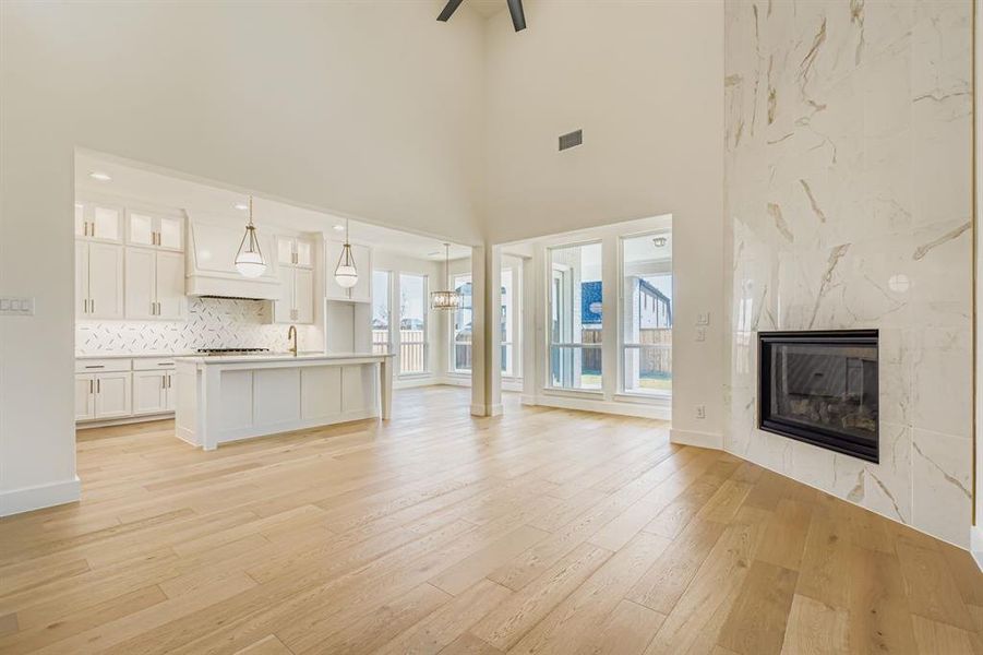 Unfurnished living room featuring a premium fireplace, light wood-type flooring, a high ceiling, and a chandelier