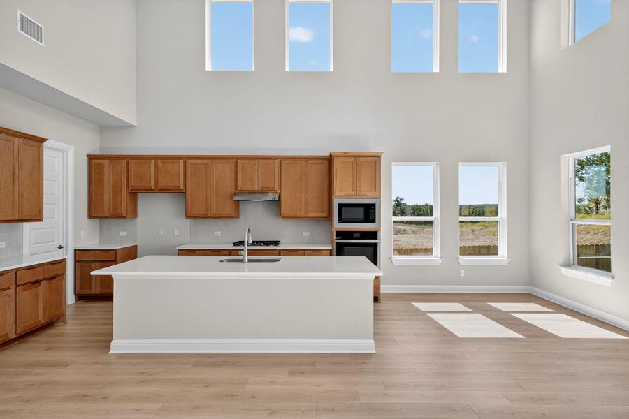 Kitchen with brown cabinetry, plenty of natural light, a high ceiling, a kitchen island with sink, and light wood-style flooring Kitchen with brown cabinetry, plenty of natural light, a high ceiling, a kitchen island with sink, and light wood-style flooring