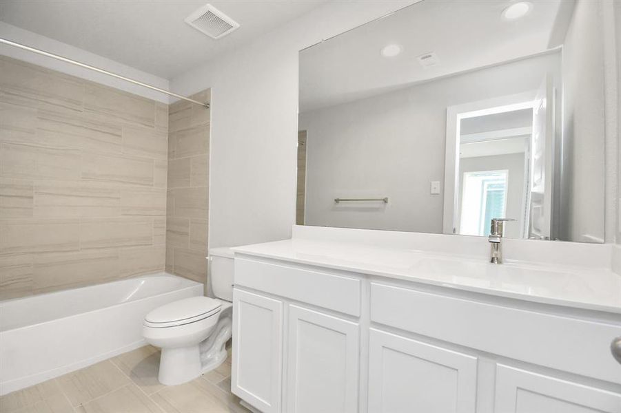 Secondary bath features tile flooring, walk-in shower with tile surround, light colored cabinets and a beautiful light countertop.