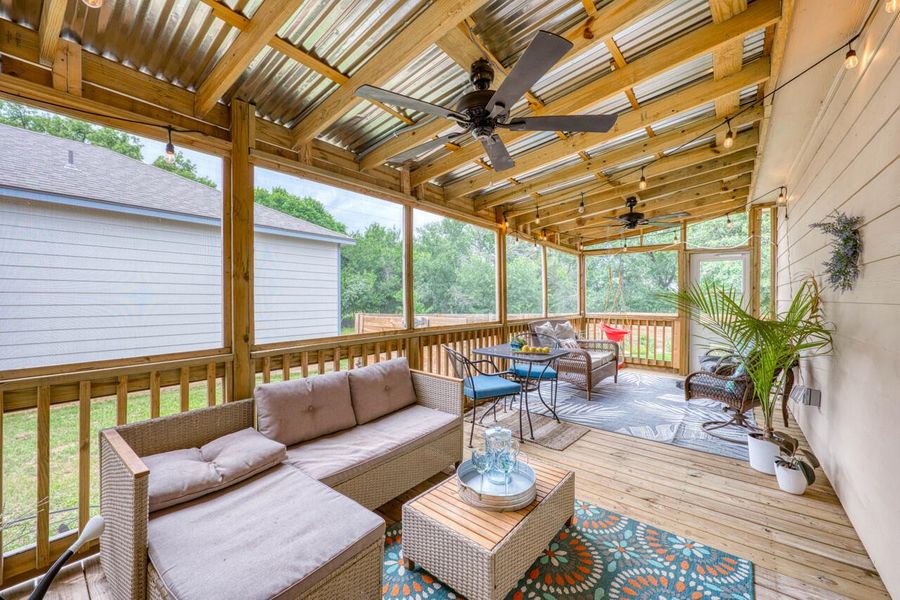 Expansive screened-in porch featuring a wood deck, exposed wood beam ceiling with corrugated metal panels, and two ceiling fans