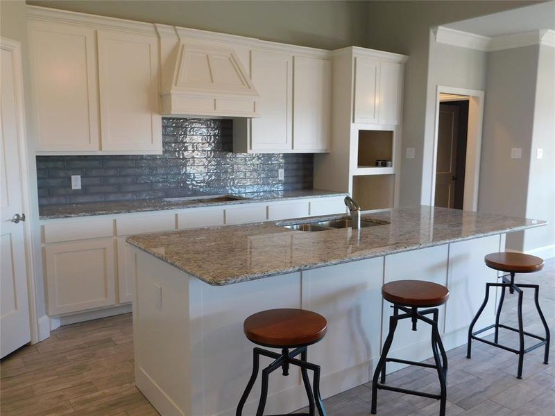 Kitchen featuring light hardwood / wood-style floors, white cabinetry, custom exhaust hood, a center island with sink, and sink