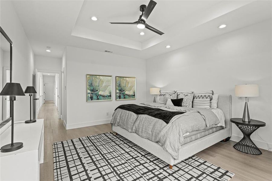 Bedroom with light hardwood / wood-style flooring, ceiling fan, and a tray ceiling