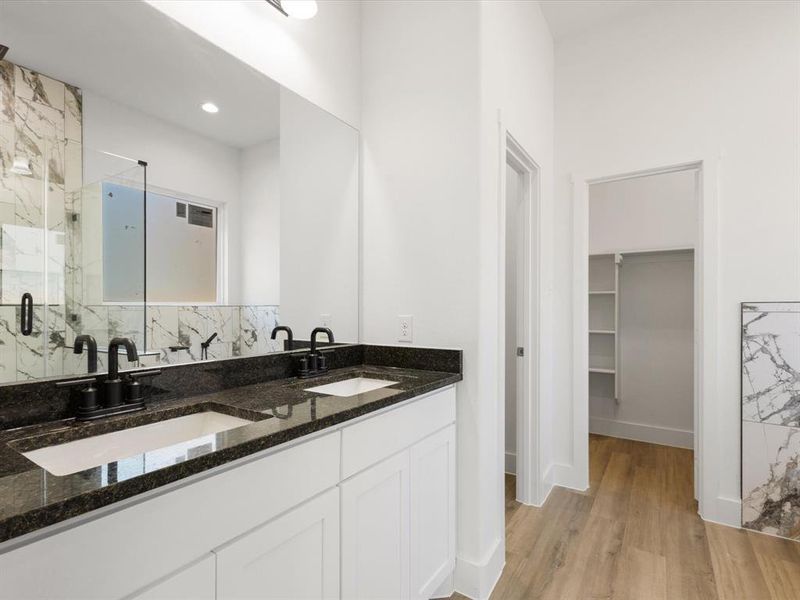 Full bath with a marble finish shower, a spacious closet, double vanity, and light wood-type flooring