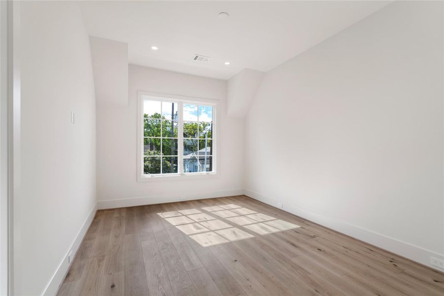 The first secondary bedroom includes front-facing windows and a bit of architectural detail. Hardwoods and high ceilings continue. A queen bed fits perfectly here. Add in an area rug to make things extra cozy.