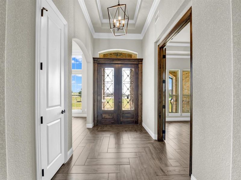 Foyer featuring french doors, a chandelier, a raised ceiling, dark parquet flooring, and ornamental molding