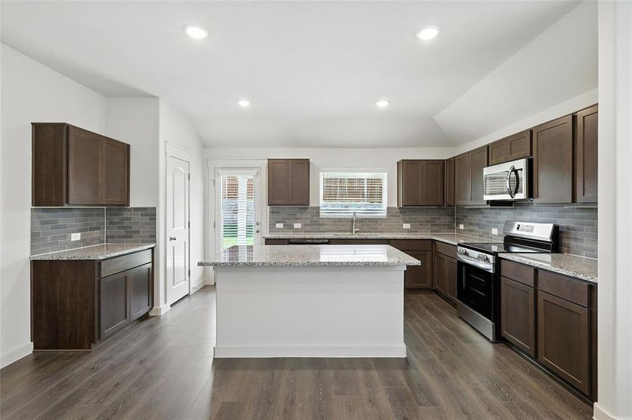 Kitchen with stainless steel appliances, dark wood finished floors, a kitchen island, decorative backsplash, and dark brown cabinets Kitchen with stainless steel appliances, dark wood finished floors, a kitchen island, decorative backsplash, and dark brown cabinets