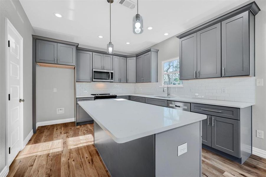 Kitchen with gray cabinetry, stainless steel appliances, sink, pendant lighting, and a center island