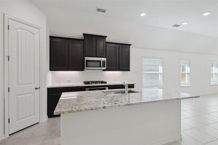 Kitchen featuring light stone counters, an island with sink, sink, tasteful backsplash, and appliances with stainless steel finishes