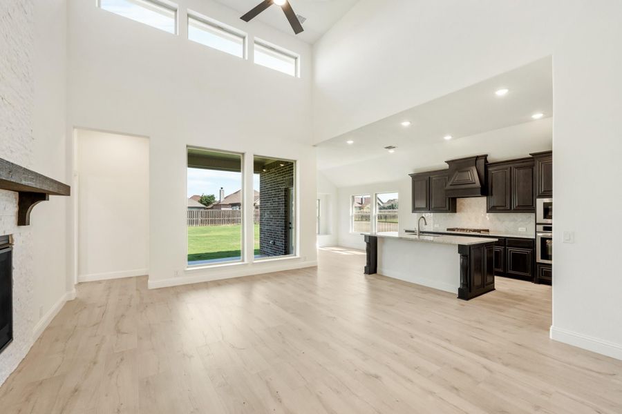 Open-plan living area with high ceilings, fireplace, and kitchen with dark cabinets and island