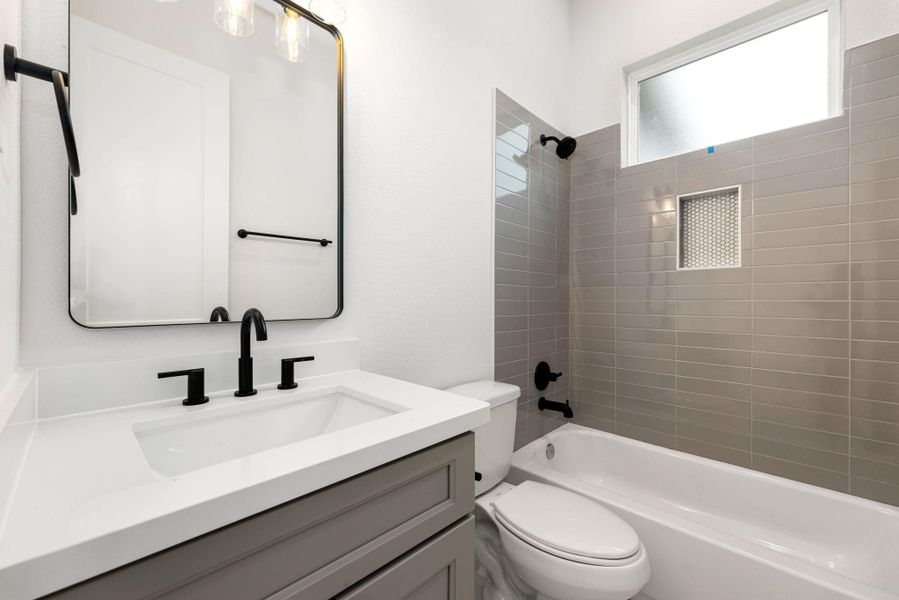 The secondary bathroom boasts elegant light countertops paired with contemporary grey cabinetry, creating a refined and airy atmosphere. The oversized walk-in shower, with its custom tile surround, offers a spa-like experience, while the decorative mirror adds a touch of sophistication. The sleek fixtures and modern finishes complement the tile floors, enhancing the bathroom’s sleek design. The secondary bathroom boasts elegant light countertops paired with contemporary grey cabinetry, creating a refined and airy atmosphere. The oversized walk-in shower, with its custom tile surround, offers a spa-like experience, while the decorative mirror adds a touch of sophistication. The sleek fixtures and modern finishes complement the tile floors, enhancing the bathroom’s sleek design.