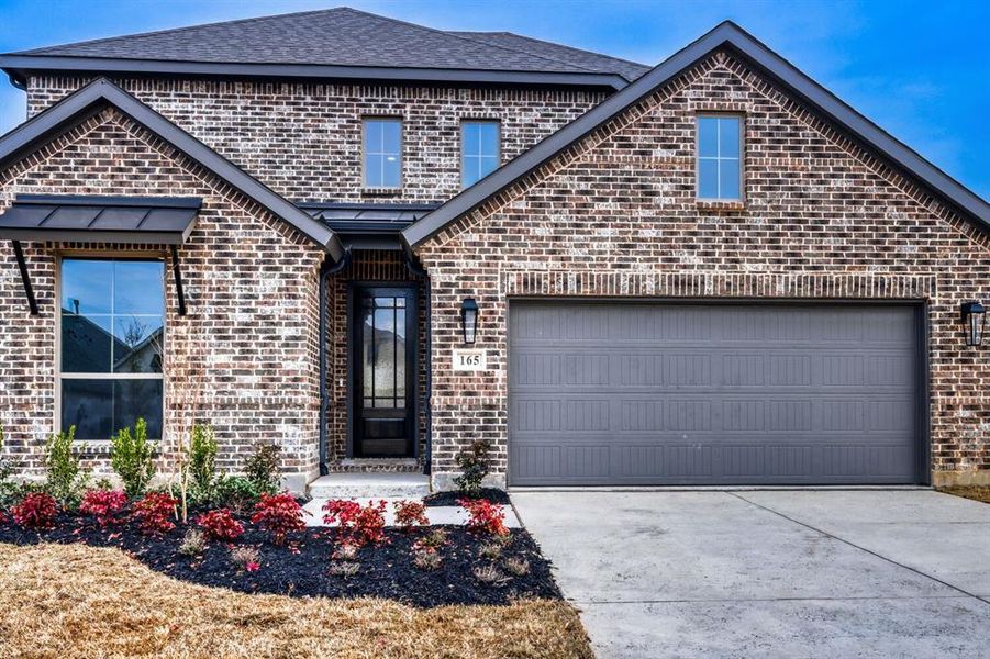 View of front of property featuring brick siding, concrete driveway, roof with shingles, and an attached garage
