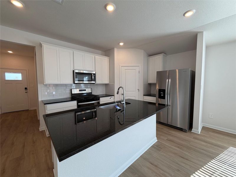 Kitchen featuring appliances with stainless steel finishes, white cabinetry, decorative backsplash, dark stone counters, and an island with sink