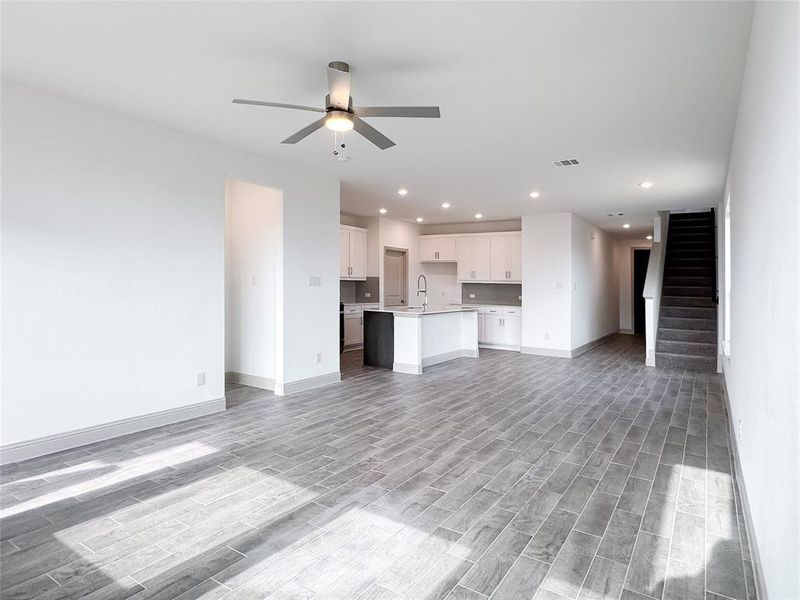 Unfurnished living room with stairway, visible vents, light wood-type flooring, and ceiling fan