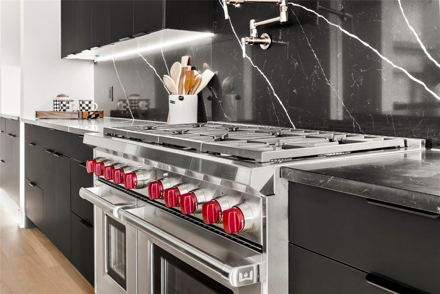 Kitchen view of dark cabinets, range with two ovens, modern cabinets, tasteful backsplash, and light wood finished floors Kitchen view of dark cabinets, range with two ovens, modern cabinets, tasteful backsplash, and light wood finished floors