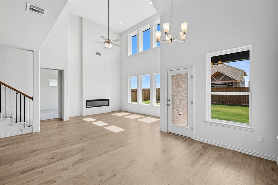 Unfurnished living room with a towering ceiling, a large fireplace, plenty of natural light, a ceiling fan, and light wood finished floors Unfurnished living room with a towering ceiling, a large fireplace, plenty of natural light, a ceiling fan, and light wood finished floors