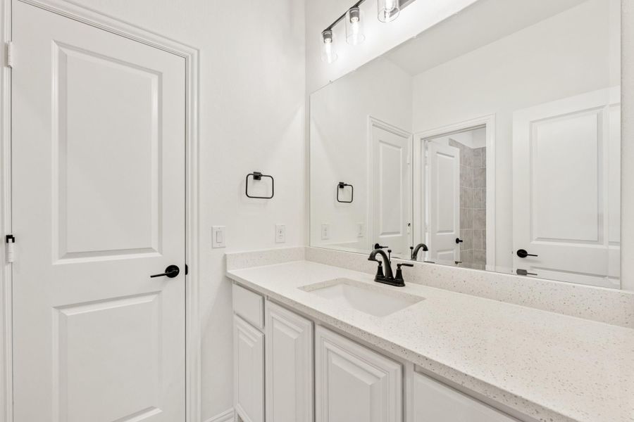 Bathroom vanity with white cabinets, quartz countertop, black faucet, and large mirror with overhead lighting