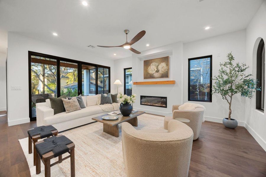 Spacious living area featuring wood-finish flooring, a contemporary fireplace with a wood mantle, and a ceiling fan