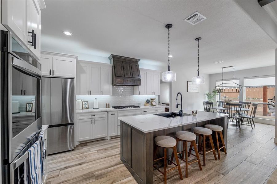 Kitchen with sink, white cabinetry, pendant lighting, stainless steel appliances, and a kitchen island with sink