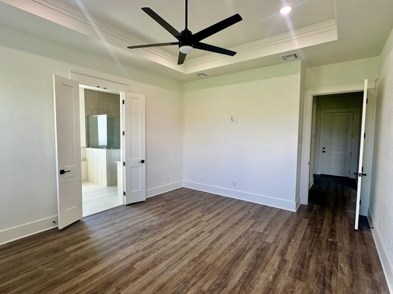 Unfurnished bedroom featuring dark wood-style floors, a tray ceiling, a ceiling fan, ensuite bathroom, and crown molding