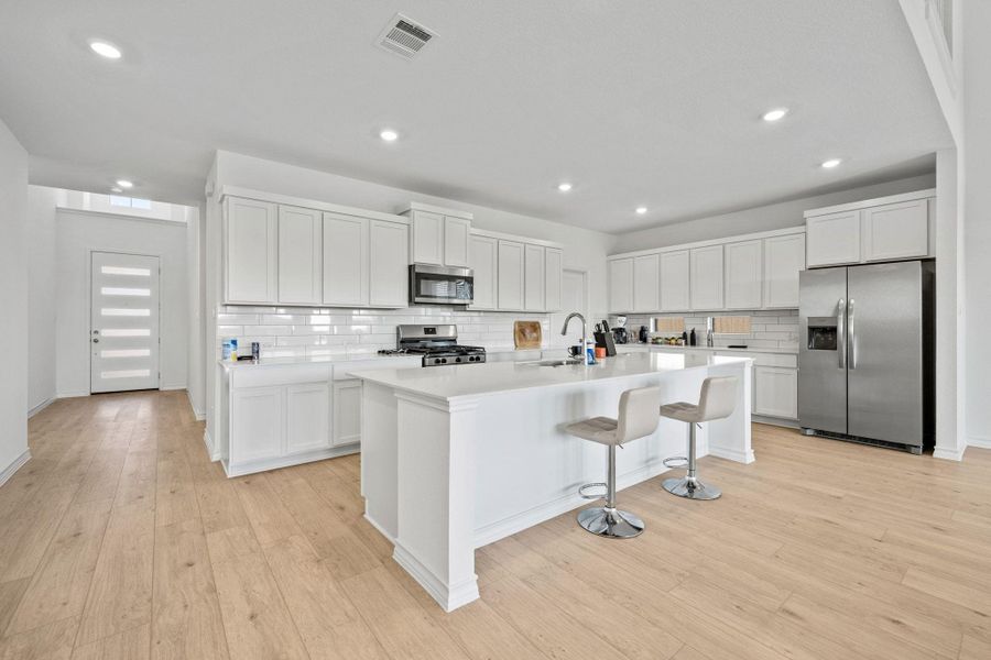Kitchen with stainless steel appliances, a breakfast bar, white cabinetry, tasteful backsplash, and a kitchen island with sink