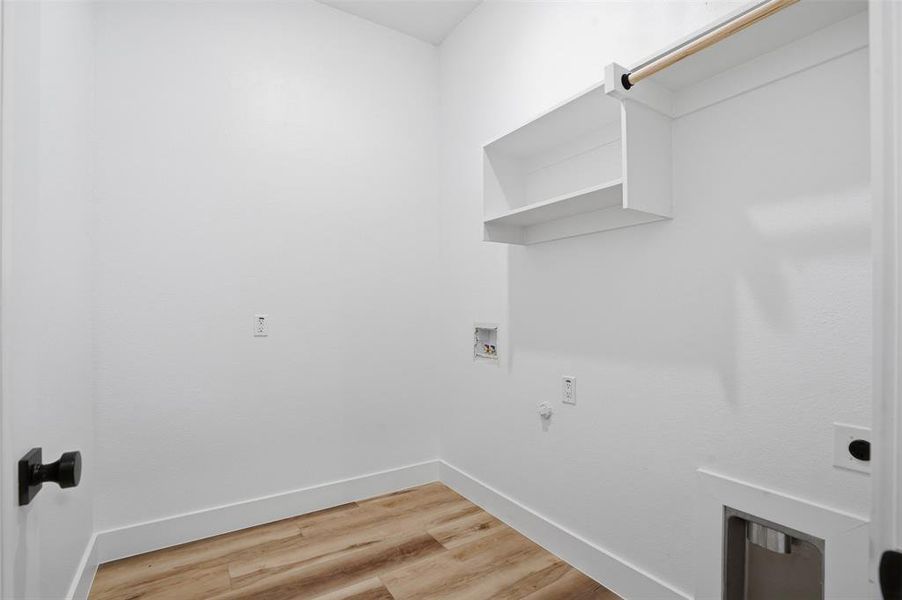 Dedicated laundry space featuring wood-finish flooring, white walls, and built-in shelving