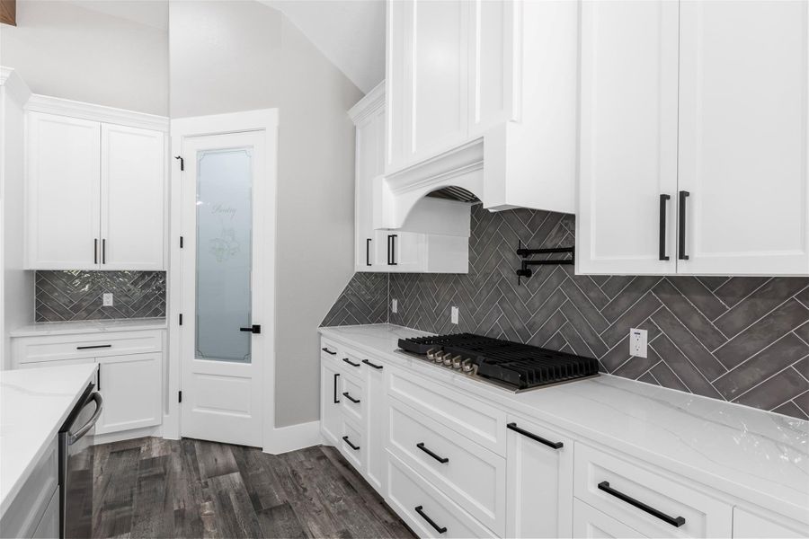 Elegant herringbone tile backsplash, and a large gas cooktop.