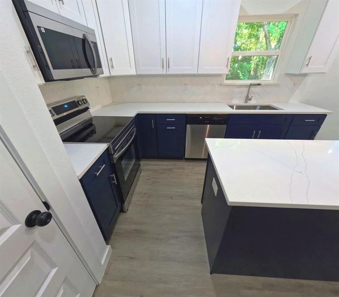 Kitchen featuring blue cabinetry, appliances with stainless steel finishes, white cabinets, light stone countertops, and tasteful backsplash Kitchen featuring blue cabinetry, appliances with stainless steel finishes, white cabinets, light stone countertops, and tasteful backsplash