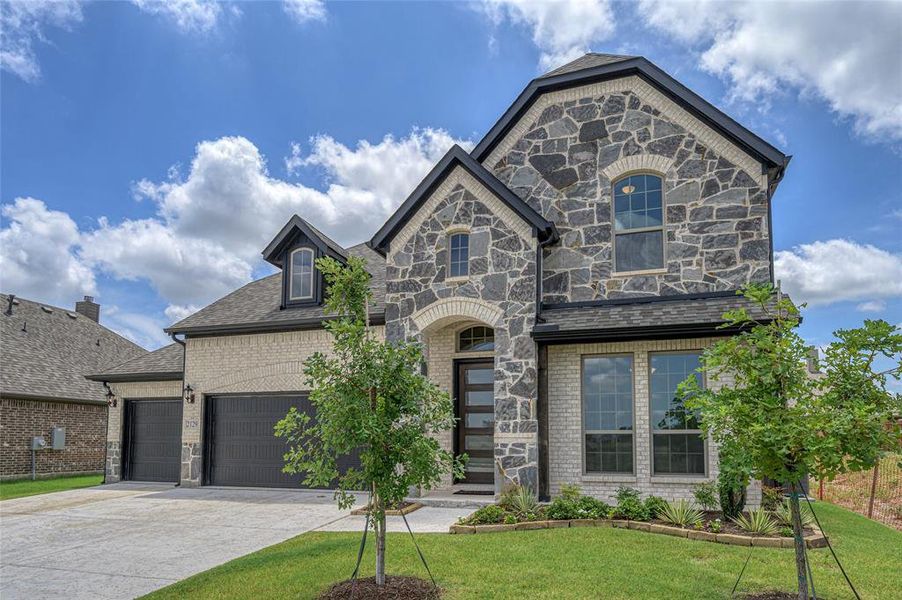 French country home featuring stone siding, driveway, brick siding, and a front lawn