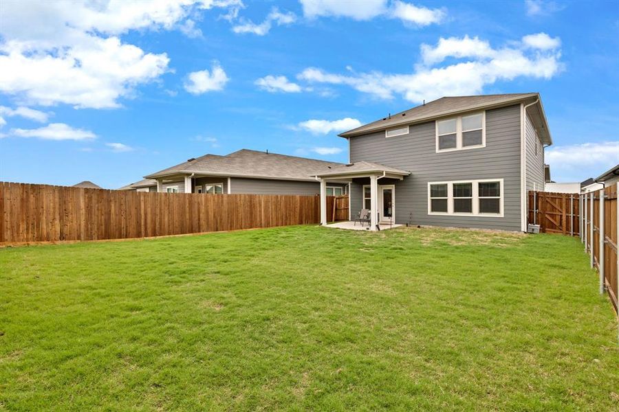 The property features a spacious lawn, a covered patio area, and a privacy fence