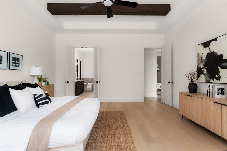 A primary bedroom offering tray ceilings and elegant hardwood flooring, with convenient access to the primary bath.