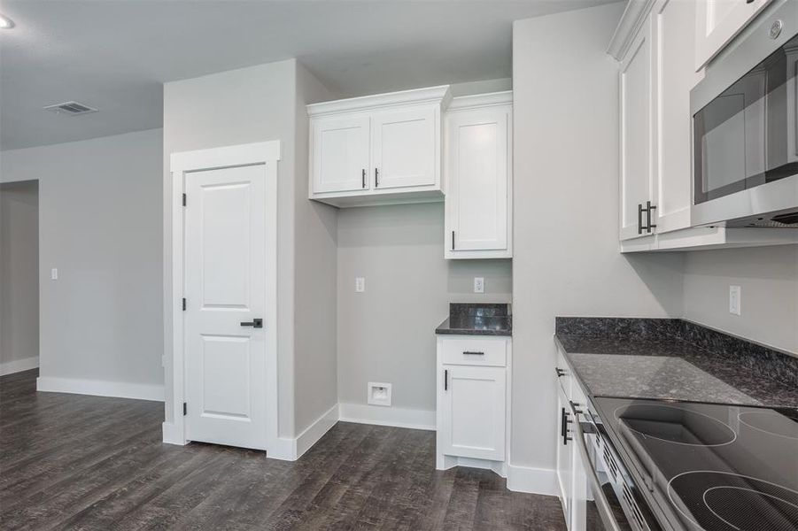 Kitchen with stainless steel appliances, dark stone countertops, white cabinetry, and dark wood-style flooring Kitchen with stainless steel appliances, dark stone countertops, white cabinetry, and dark wood-style flooring