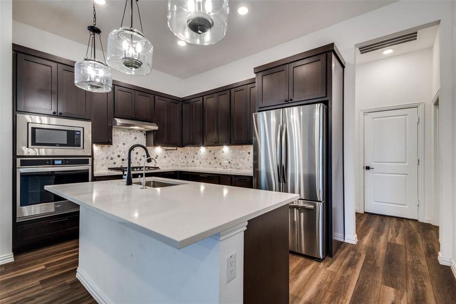 Kitchen with dark hardwood / wood-style floors, a center island with sink, stainless steel appliances, and dark brown cabinets