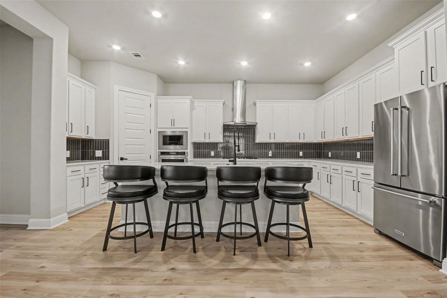 Spacious modern kitchen with sleek white cabinetry, stainless steel appliances, and a large island with seating for four. The room is well-lit with recessed lighting, and features a stylish backsplash and wood flooring. Spacious modern kitchen with sleek white cabinetry, stainless steel appliances, and a large island with seating for four. The room is well-lit with recessed lighting, and features a stylish backsplash and wood flooring.