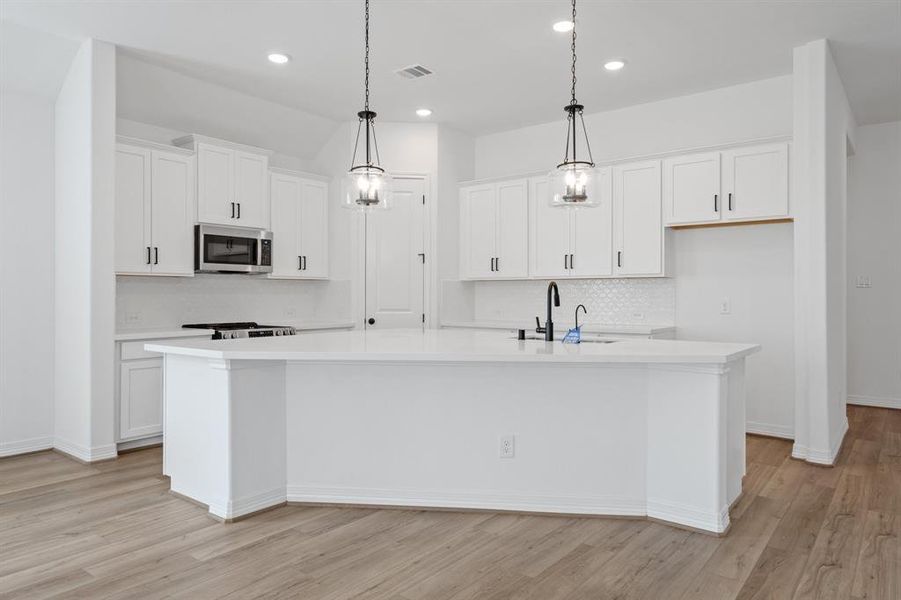 This light and bright kitchen features a large quartz island, white cabinets, a large sink overlooking your family room, recessed lighting, and beautiful backsplash.