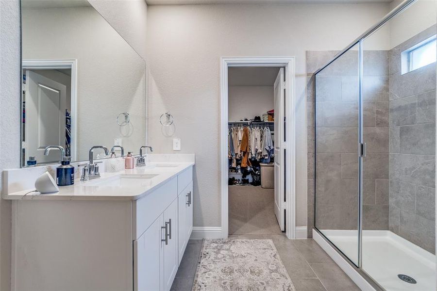 Bathroom with a spacious closet, double vanity, a stall shower, and light tile patterned floors Bathroom with a spacious closet, double vanity, a stall shower, and light tile patterned floors