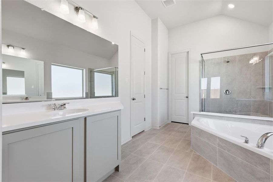 Bathroom featuring a dual vanity with light gray cabinetry, a large built-in mirror, an integrated soaking tub, a glass-enclosed shower with tiled walls, and light-toned tile flooring