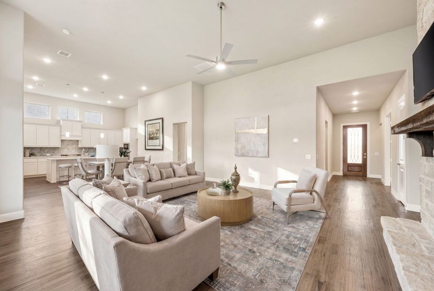 Open-concept living room with high ceilings, hardwood floors, stone fireplace, and view into kitchen