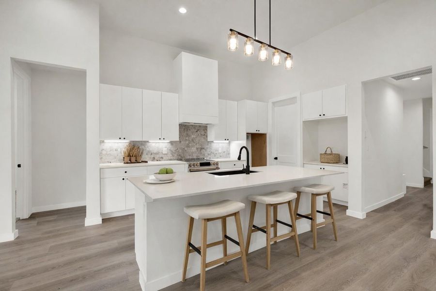 Kitchen featuring a breakfast bar area, hanging light fixtures, white cabinets, a high ceiling, and an island with sink
