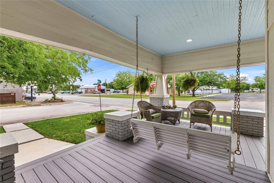 Expansive covered front porch featuring a porch swing, planked ceiling with recessed lighting, and composite decking