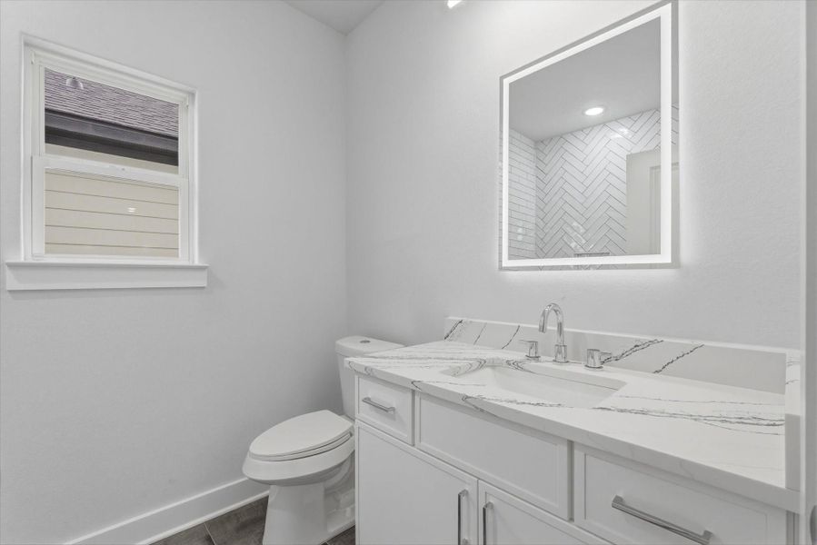 The second full bathroom upstairs features a shower/tub combination, complemented by neutral, sleek finishes and backlit vanity mirrors.