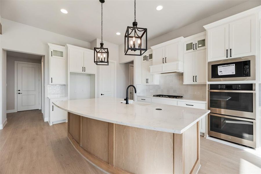 Kitchen featuring glass insert cabinets, tasteful backsplash, an island with sink, light stone counters, and stainless steel appliances Kitchen featuring glass insert cabinets, tasteful backsplash, an island with sink, light stone counters, and stainless steel appliances