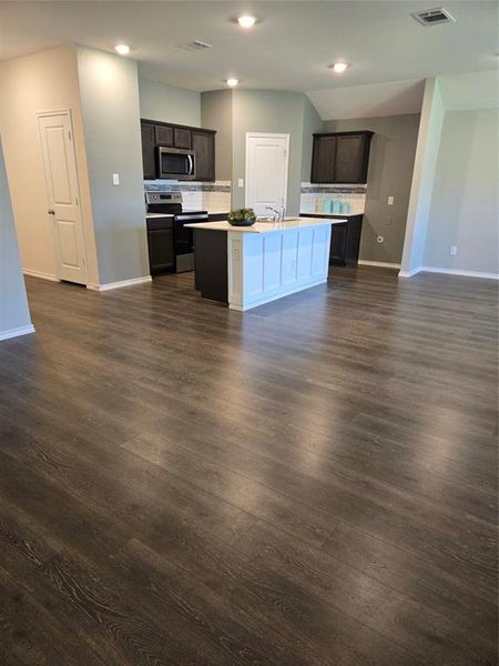 Kitchen featuring a kitchen island with sink, range, dark brown cabinets, and dark hardwood / wood-style flooring