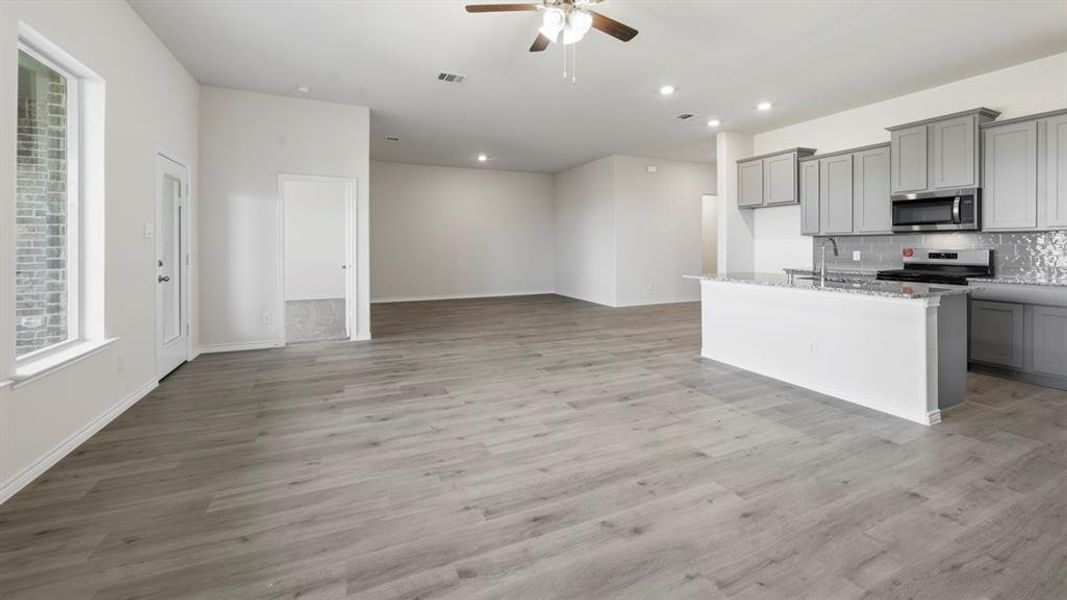 Kitchen featuring gray cabinetry, an island with sink, light stone counters, stainless steel appliances, and ceiling fan Kitchen featuring gray cabinetry, an island with sink, light stone counters, stainless steel appliances, and ceiling fan